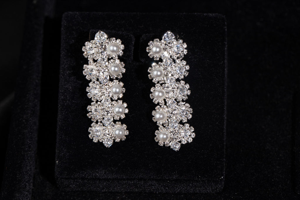Pair of silver-tone drop earrings featuring tiny zircon flower clusters and white faux pearls on black velvet.