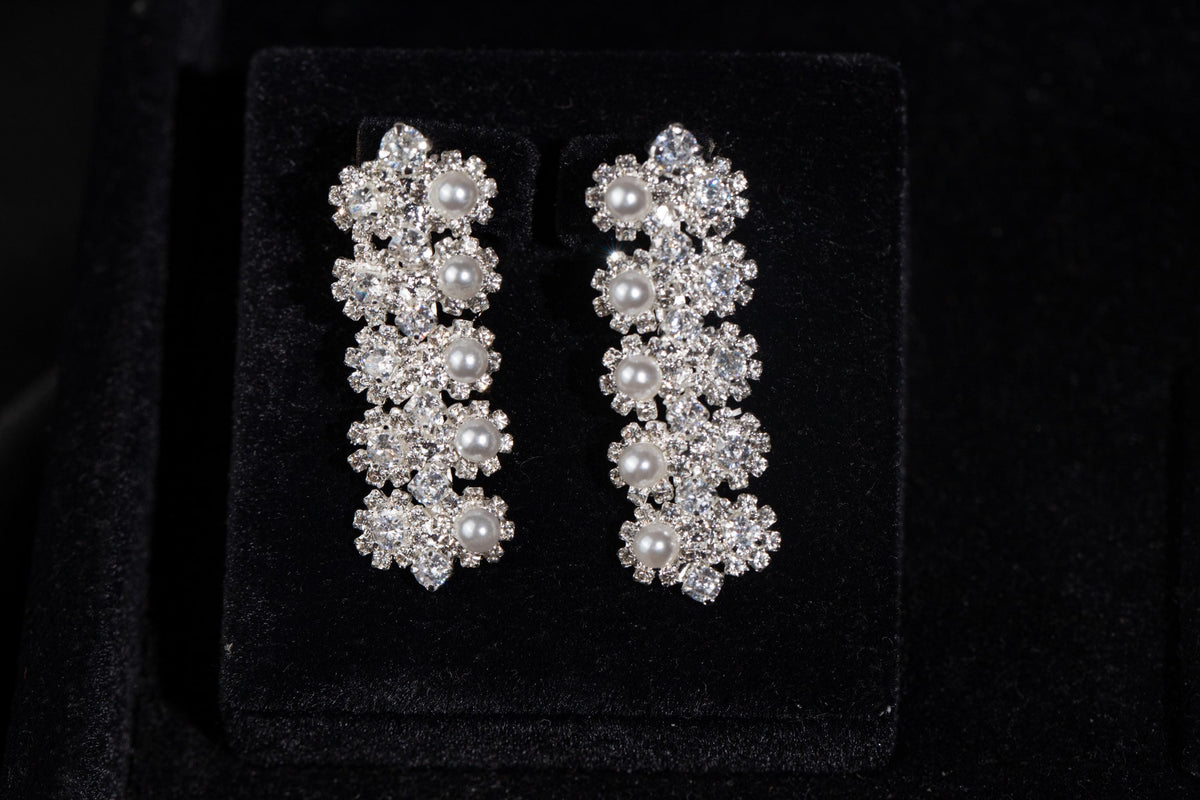 Pair of silver-tone drop earrings featuring tiny zircon flower clusters and white faux pearls on black velvet.