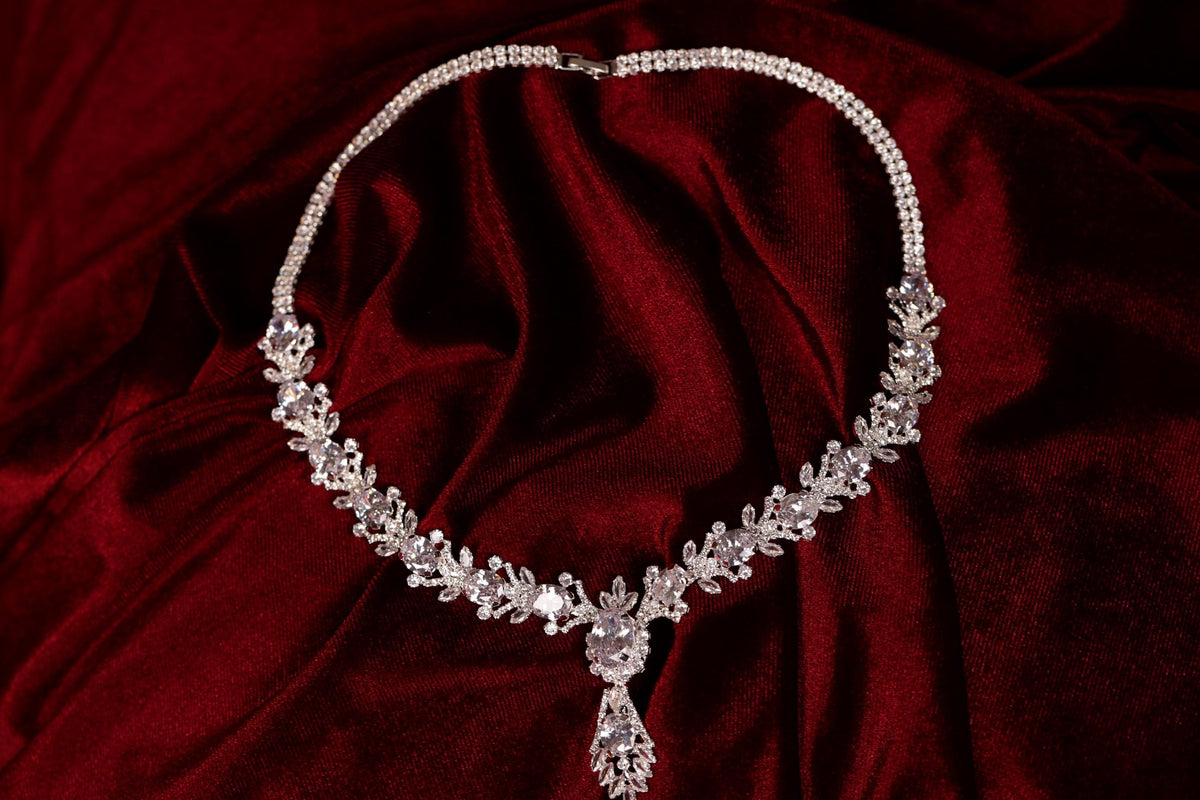 Silver-tone statement necklace with clear stones and an ornate teardrop pendant on red fabric