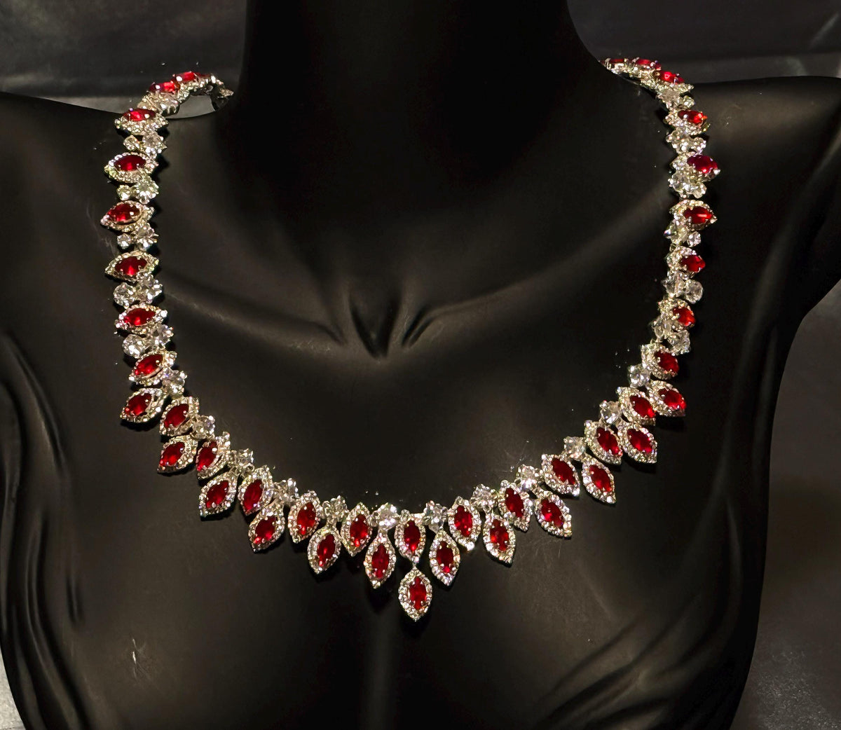 Red zircon statement necklace on a black bust, showing its graduated arrangement of oval stones and clear halo borders.