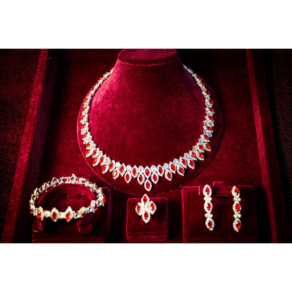 Red oval zircon necklace with matching bracelet, clustered ring and three-stone drop earrings in a burgundy velvet box.