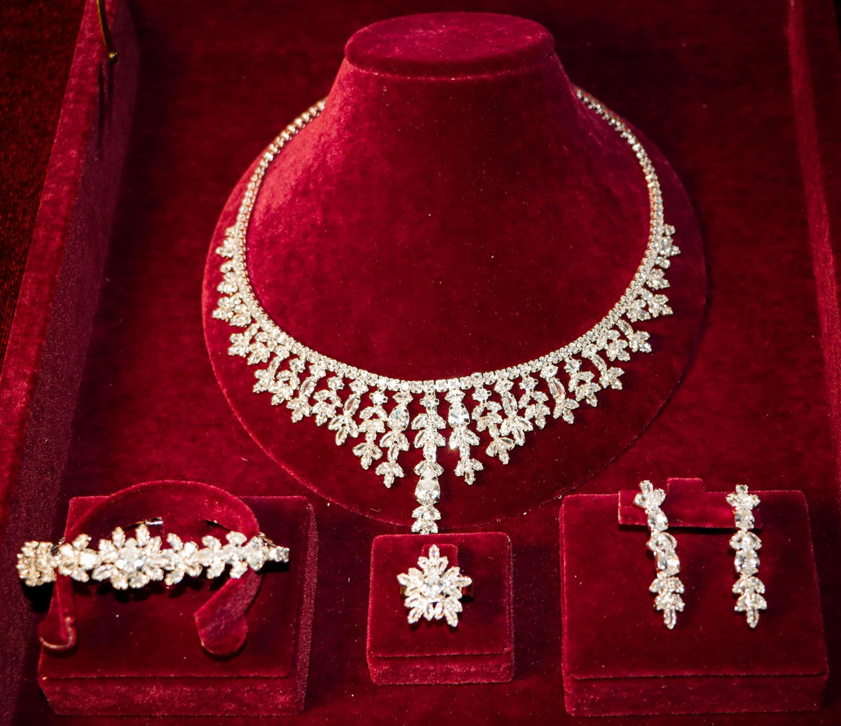 Angled view of a silver-tone cascading bridal necklace and coordinating floral bracelet, ring and earrings in a velvet box.