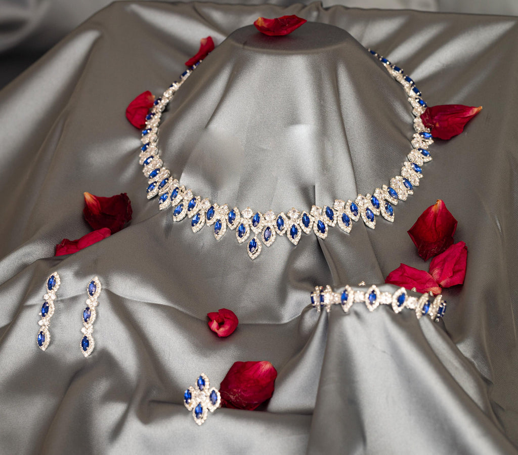 Blue zircon necklace, earrings, bracelet and ring arranged on draped gray satin with red rose petals.