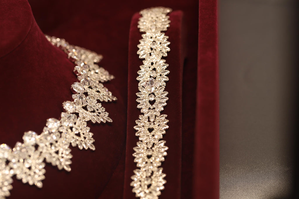 Close-up of a silver-tone crystal bracelet beside the matching necklace, showing their repeating ornamental motifs
