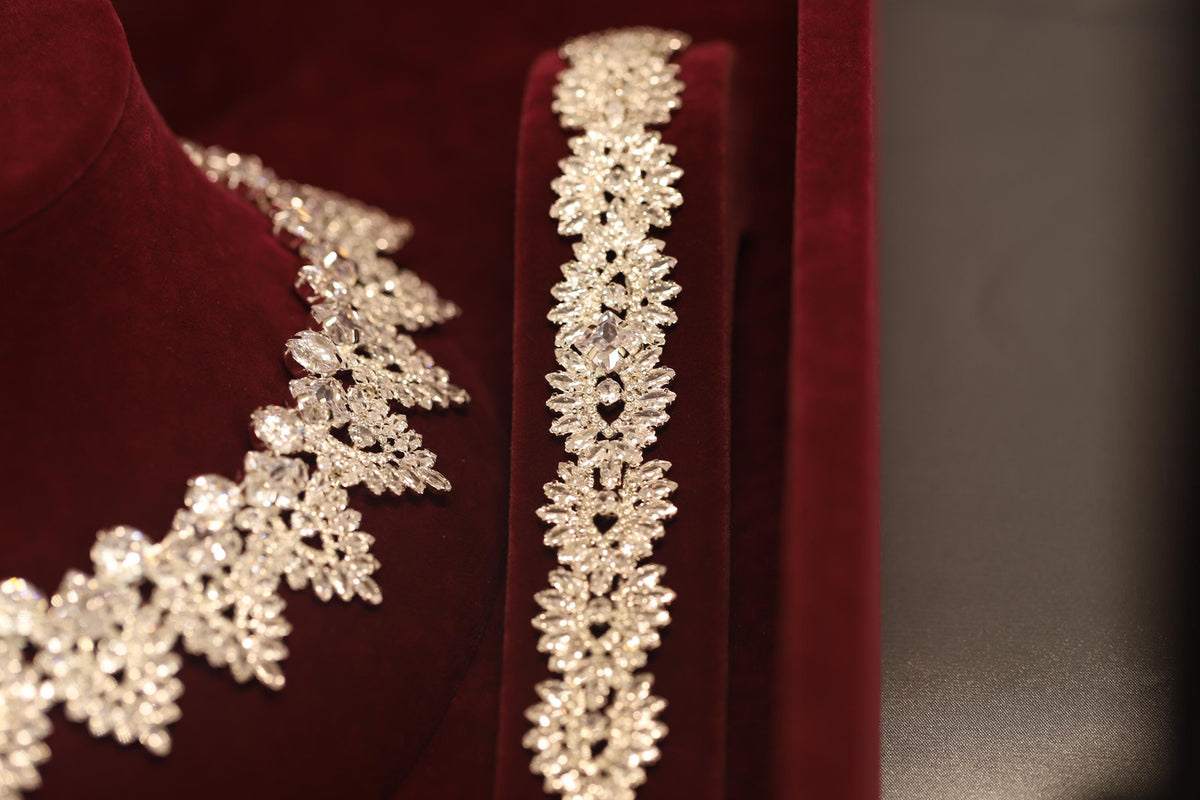 Close-up of a silver-tone crystal bracelet beside the matching necklace, showing their repeating ornamental motifs
