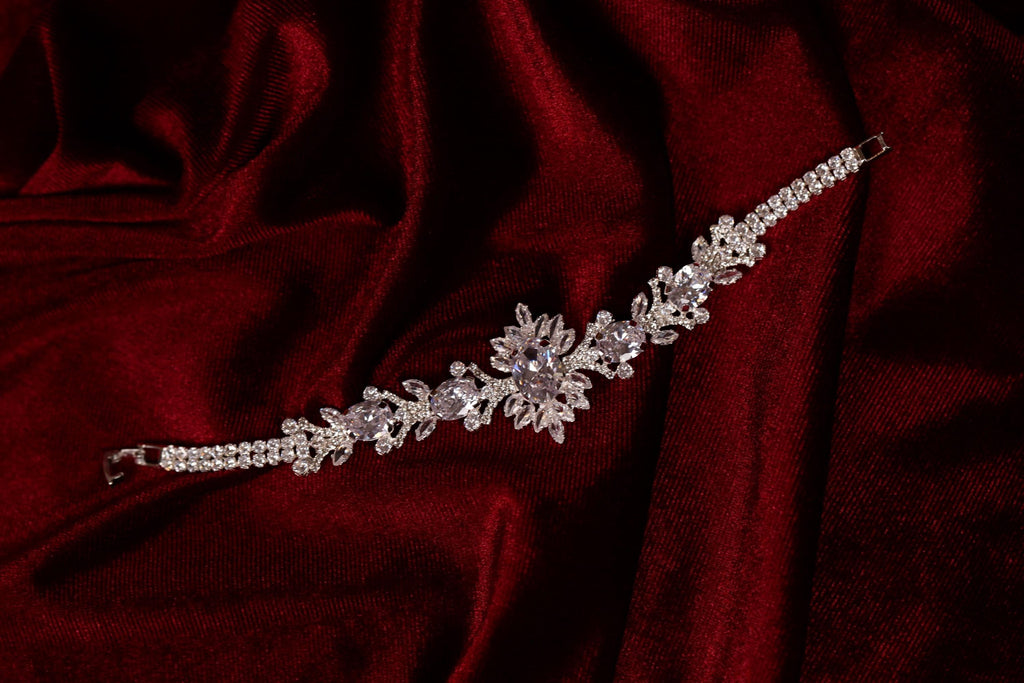 Silver-tone bracelet with clear stones and an intricate central design displayed on red fabric
