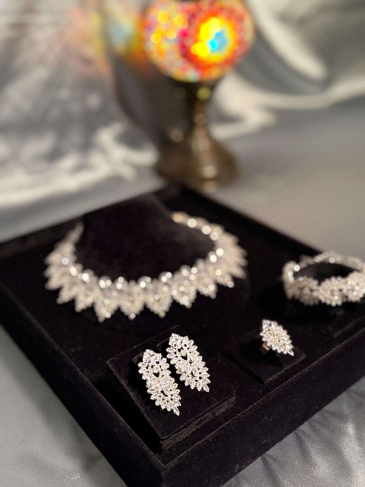Angled view of a silver-tone bridal jewelry set in a black velvet display box beside a window
