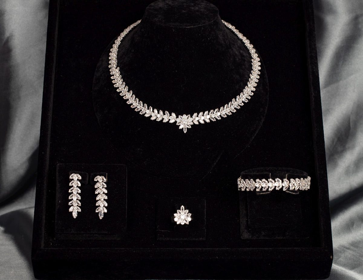 Four-piece leaf and flower bridal jewelry set arranged in a black velvet box, with a necklace, earrings, bracelet and ring.