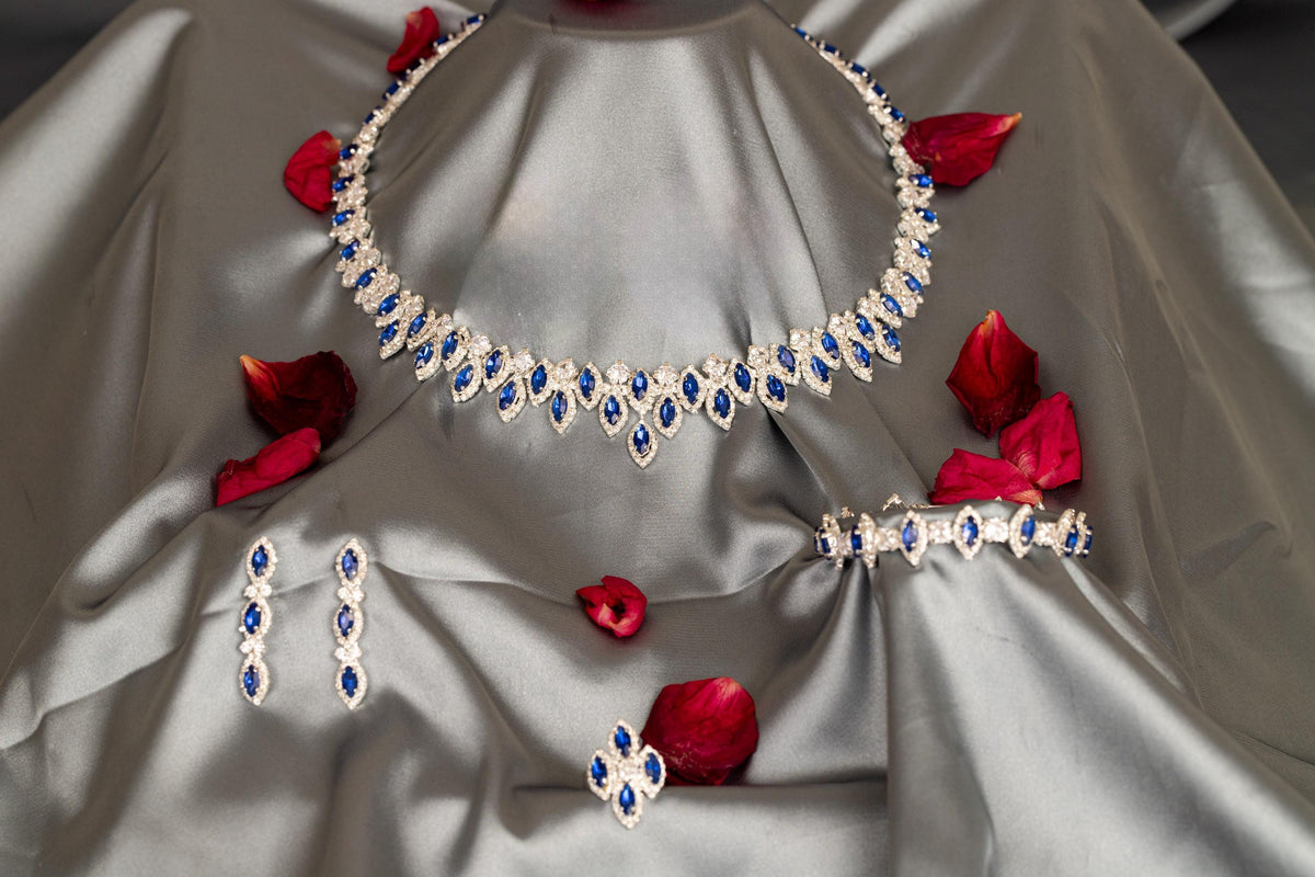 Full view of a blue zircon evening jewelry set on silver-gray satin, with matching accessories below the statement necklace.