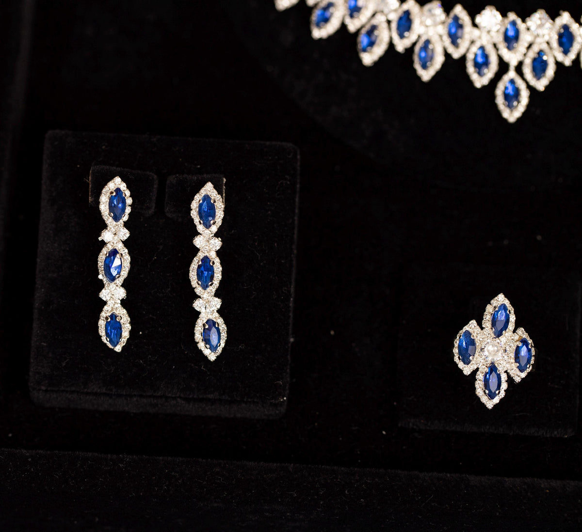 Three-stone blue zircon drop earrings and a matching four-stone cluster ring beneath the coordinating halo necklace.