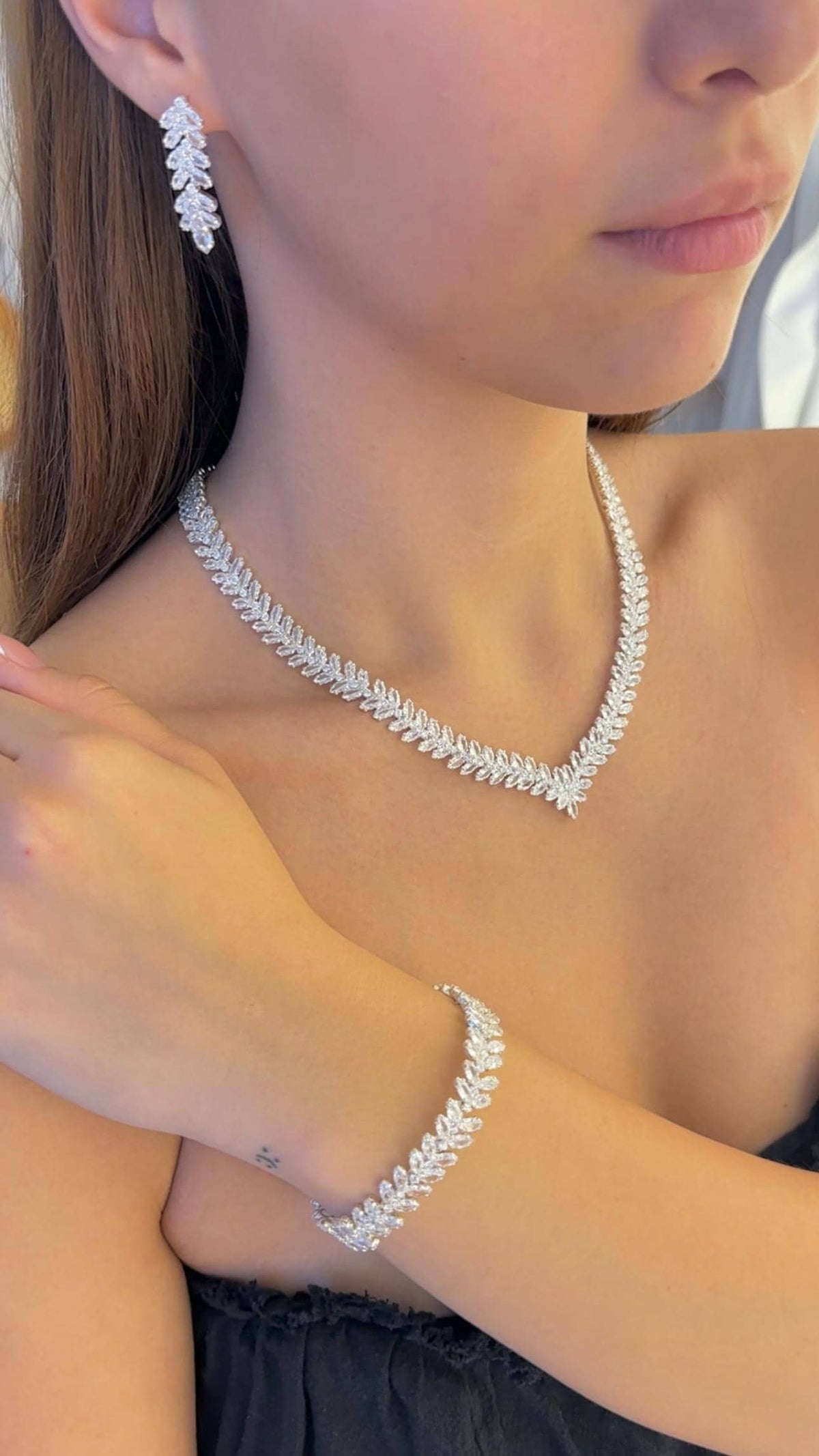 Close-up of a model wearing a zircon leaf necklace with a floral center, matching drop earrings and a leaf bracelet.