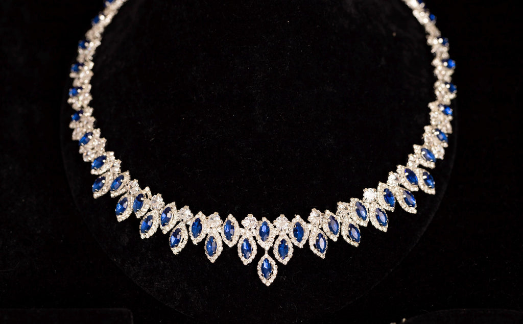 Close-up of a blue zircon statement necklace with clear halo borders and a graduated central drop on black velvet.