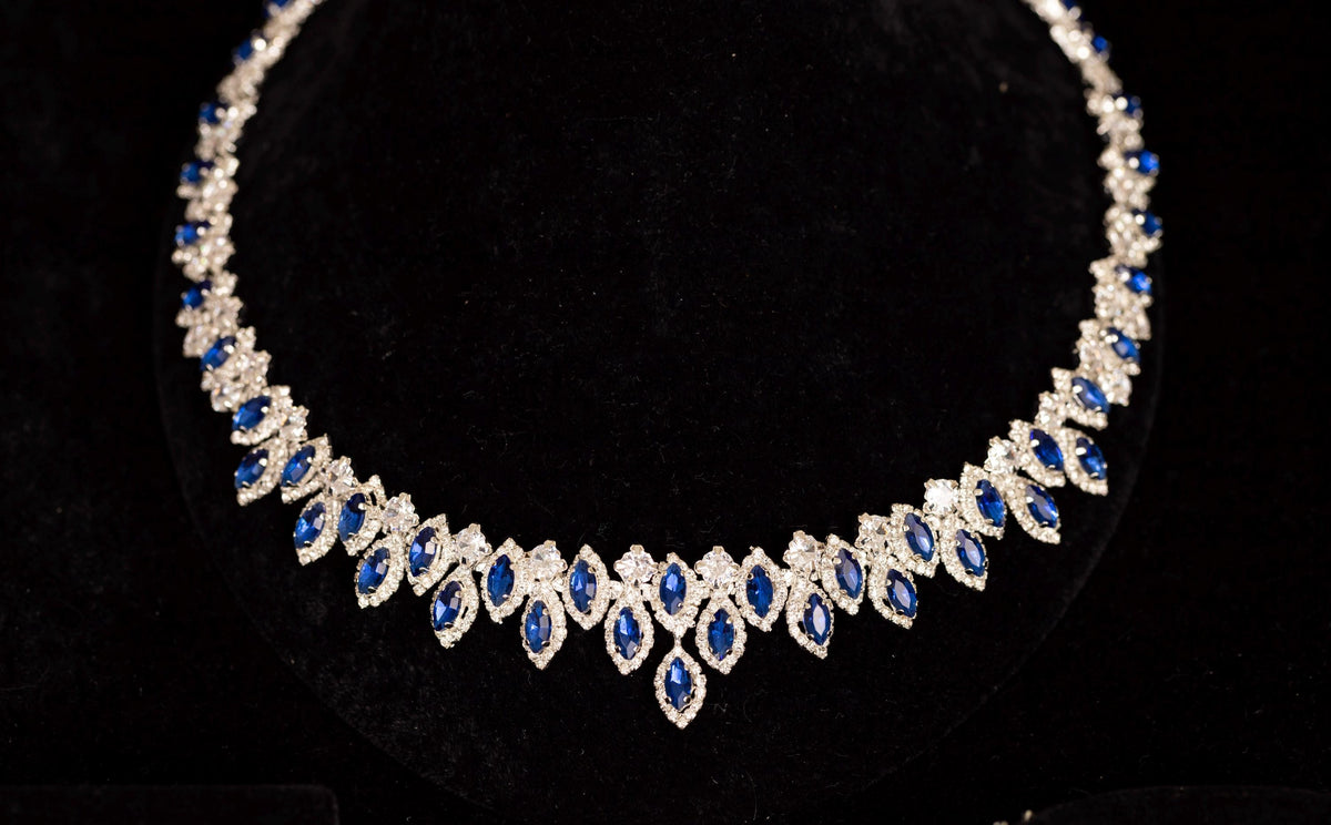 Close-up of a blue zircon statement necklace with clear halo borders and a graduated central drop on black velvet.