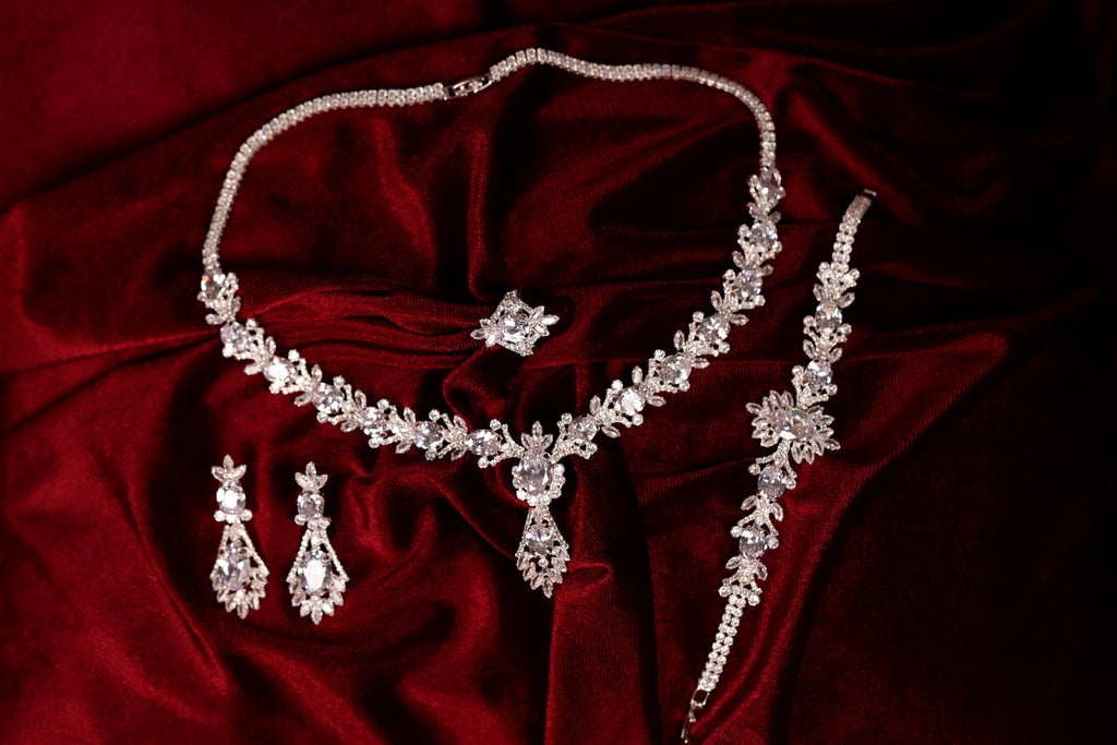 Silver-tone teardrop necklace, drop earrings, bracelet and ring arranged together on red fabric