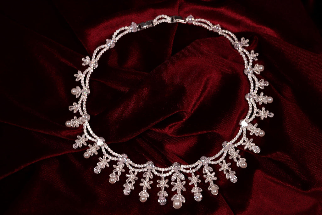 Silver floral cubic zirconia necklace with dangling pearl accents displayed on red satin