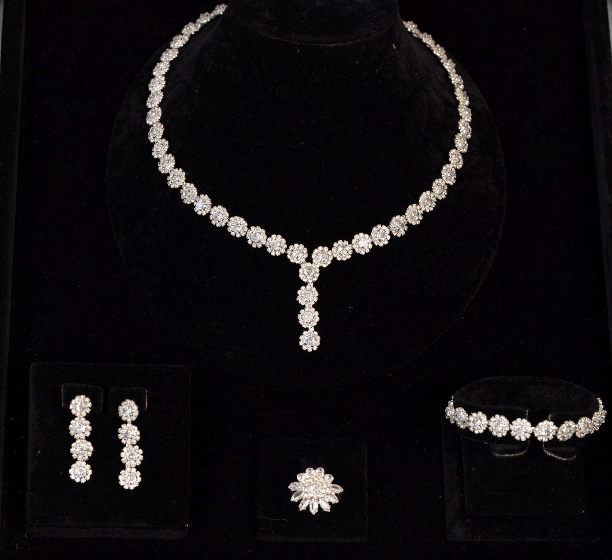 Four-piece silver-tone bridal jewelry set with miniature zircon flowers, displayed together on black velvet.