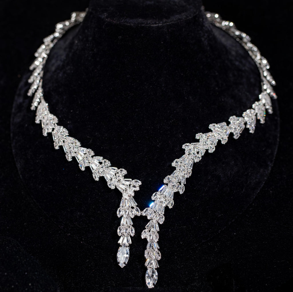 Front view of a baguette zircon necklace with repeating fan-shaped motifs and two pear-tipped drops on a black velvet bust.