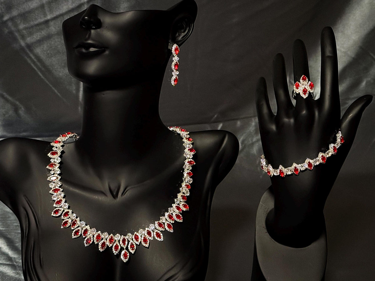 Silver-tone red zircon jewelry set on a black bust and hand stand, showing the necklace, earrings, bracelet and ring.