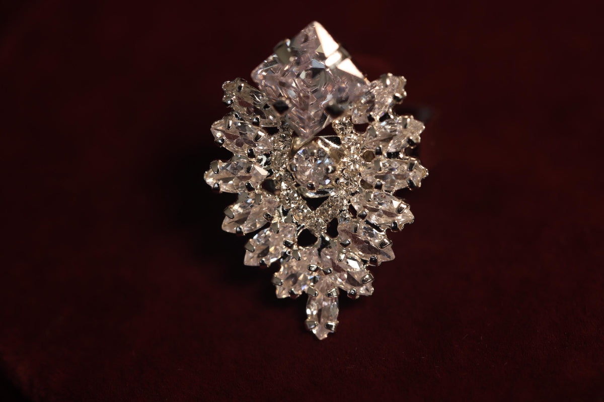 Close-up of a silver-tone statement ring with an ornate marquise-shaped crystal motif against burgundy velvet
