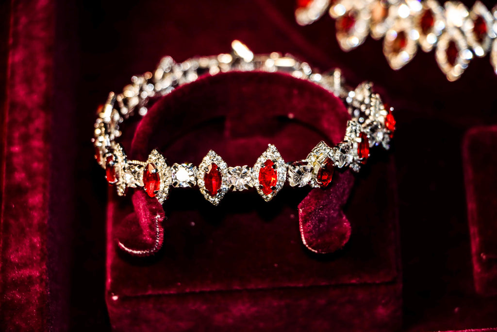 Red zircon bracelet featuring oval stones surrounded by clear sparkling halos, displayed on a burgundy velvet stand.