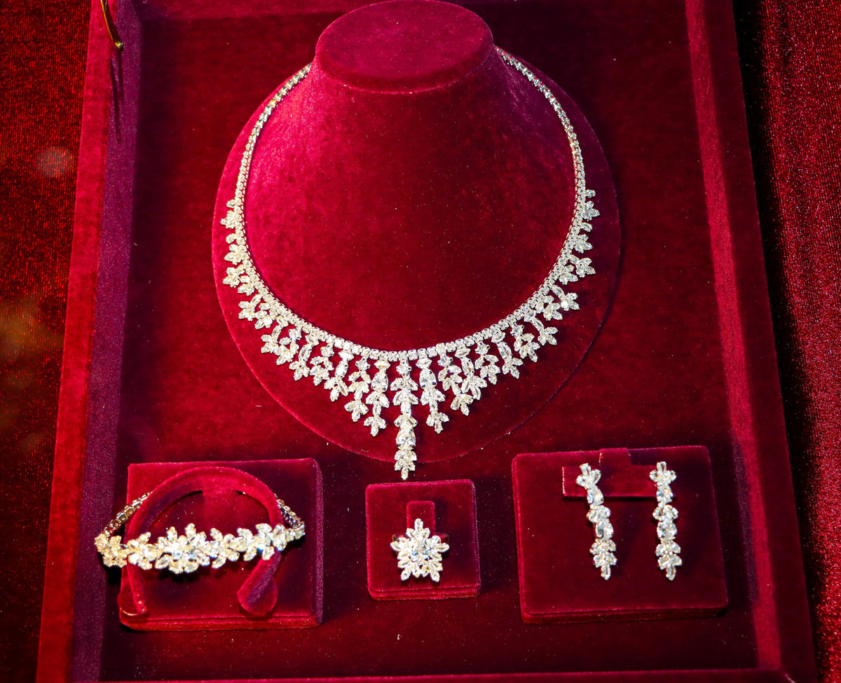 Four-piece floral bridal jewelry set arranged in a burgundy velvet box with a necklace, bracelet, ring and drop earrings.