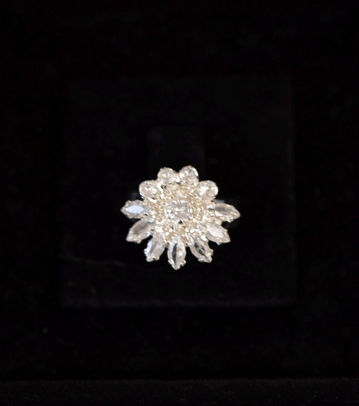 Close-up of a silver-tone floral ring with a sparkling zircon center surrounded by pointed stone petals.