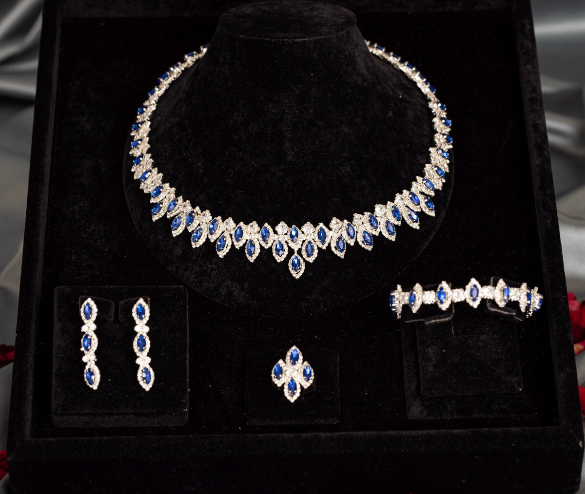 Silver-tone blue zircon halo necklace with matching earrings, bracelet and ring arranged in a black presentation box.