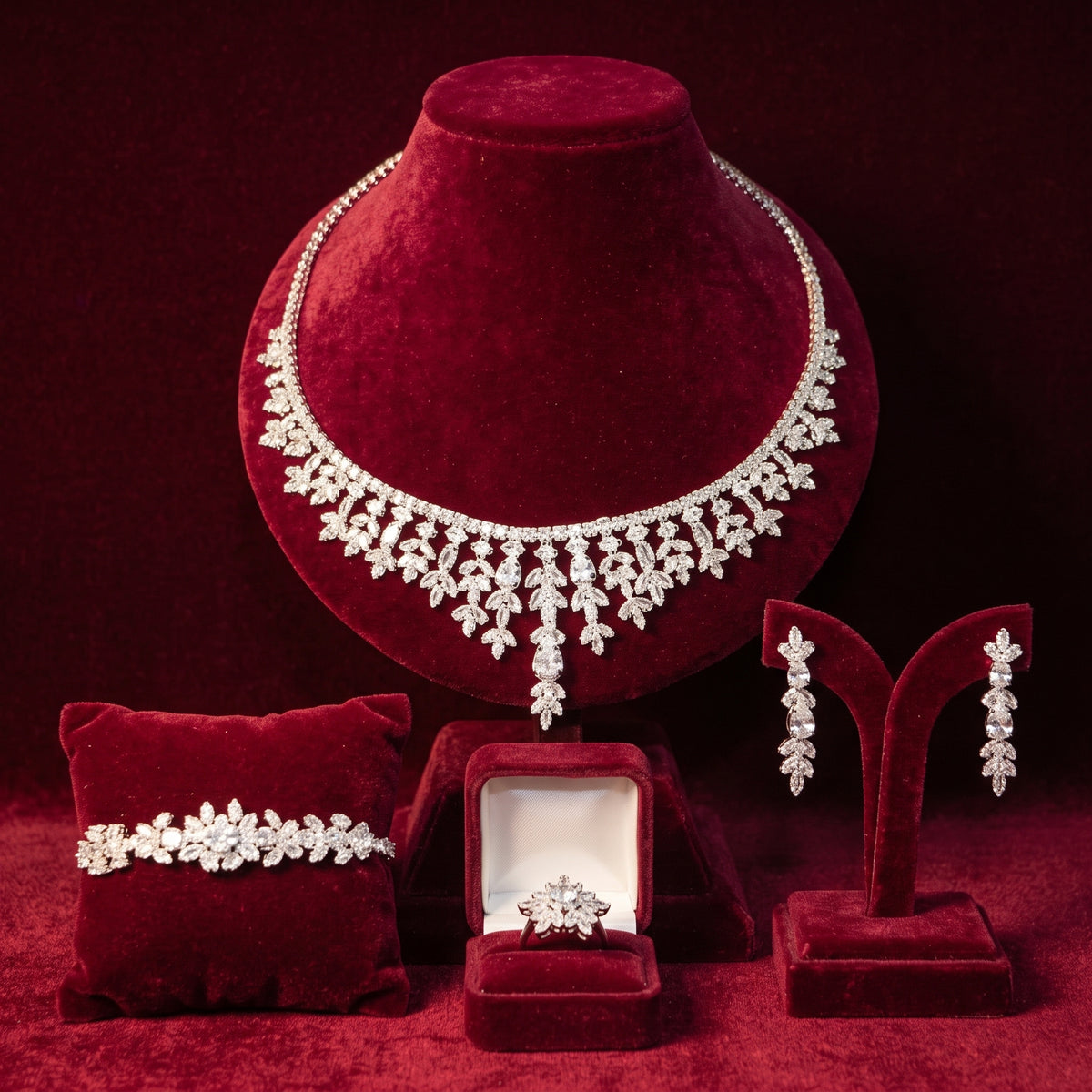 Silver-tone floral necklace with graduated teardrop details, matching earrings, bracelet and ring on burgundy velvet stands.