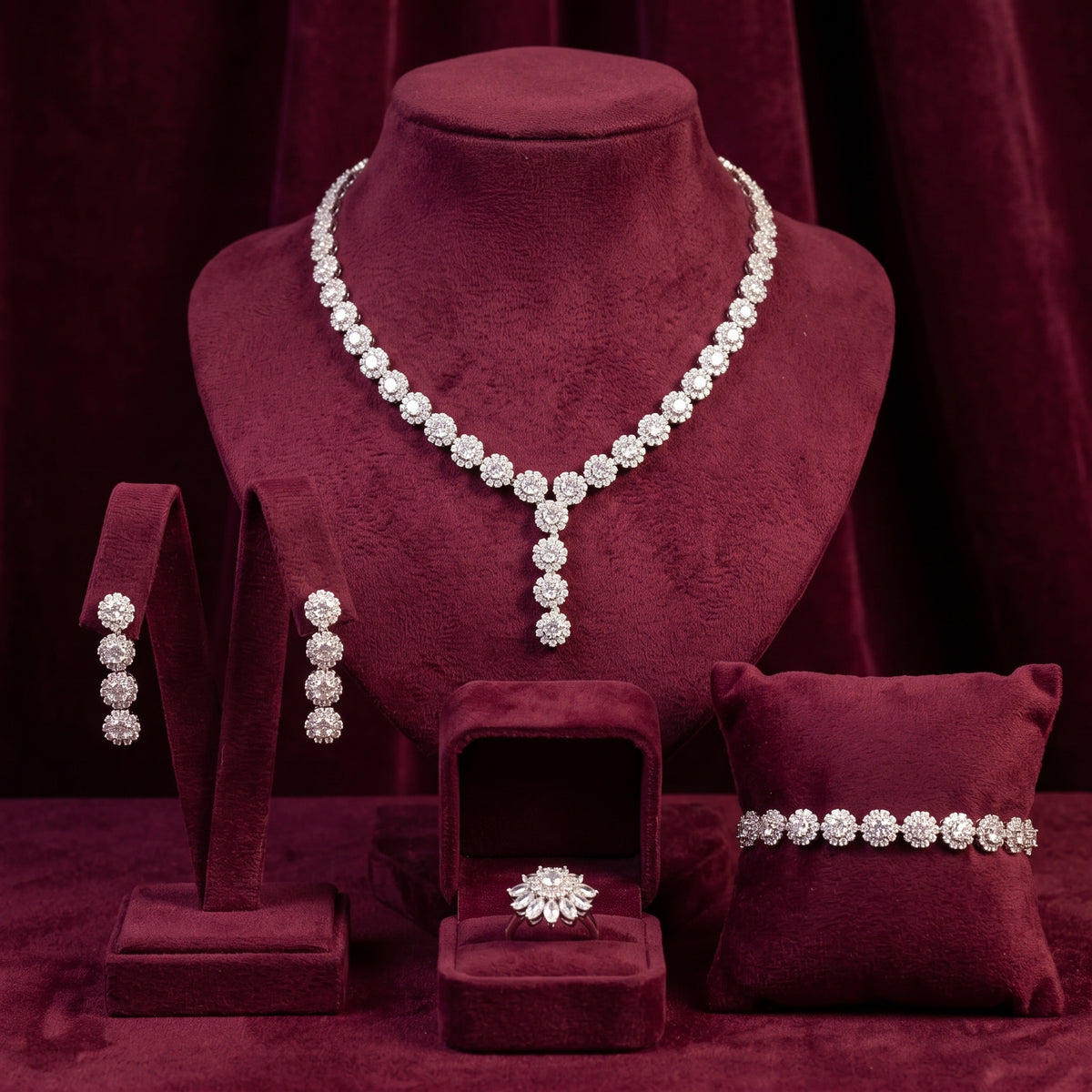 Silver-tone zircon flower necklace, earrings, bracelet and floral ring arranged on burgundy velvet jewelry stands.