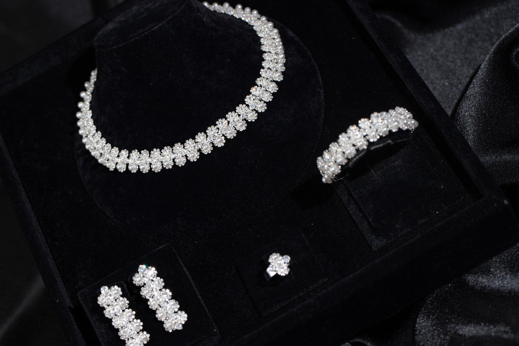 Angled view of a silver-tone floral and faux pearl necklace, earrings, bracelet and ring in a black display box.