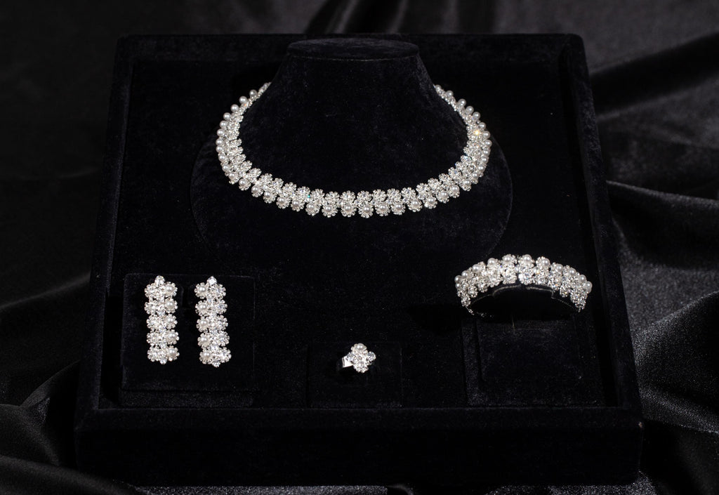 Four-piece floral bridal jewelry set with white faux pearls and zircon stones arranged in a black velvet display box.