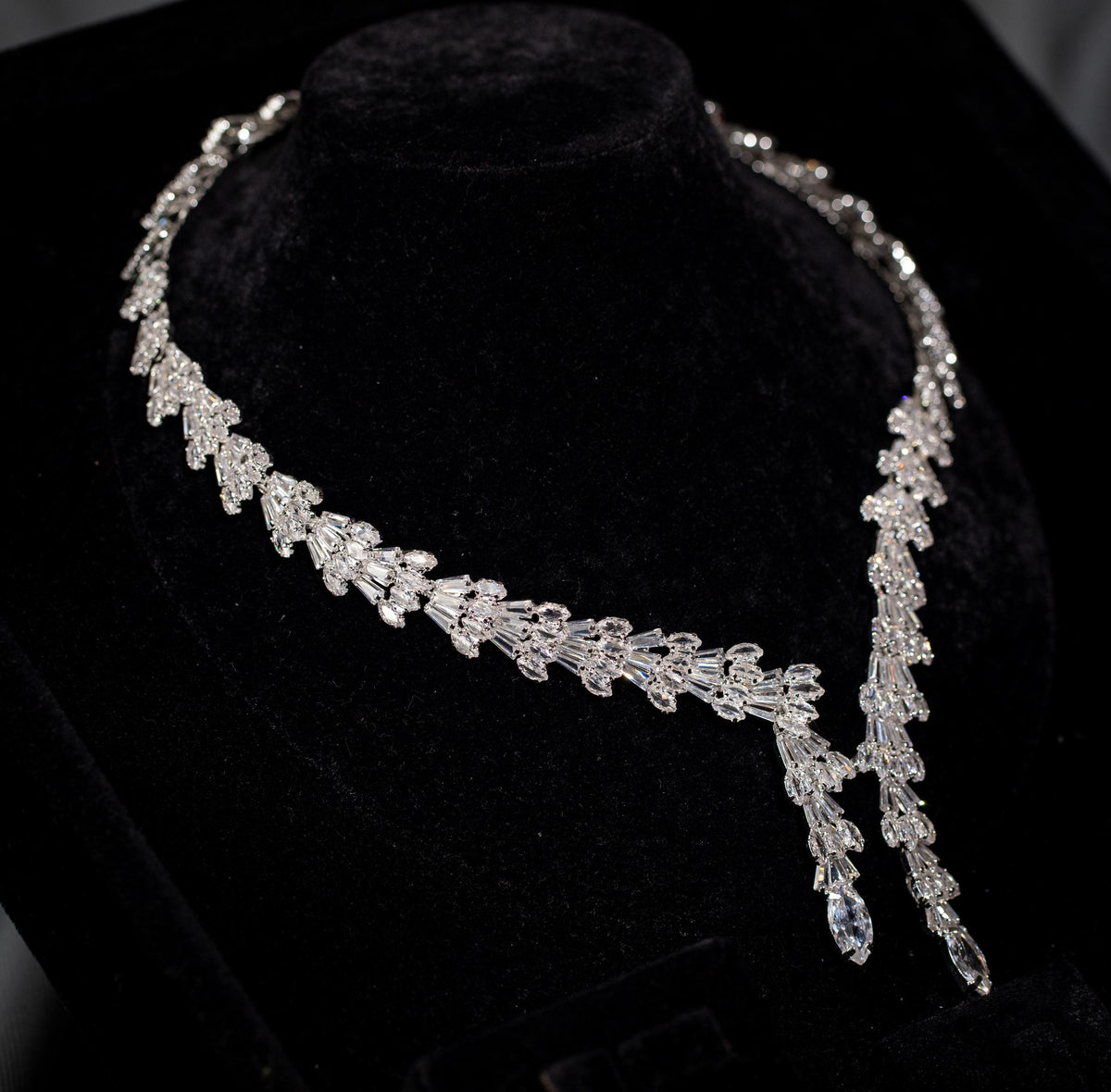 Angled view of a silver-tone bridal necklace with intricate baguette zircon details and two pendant drops of different lengths.