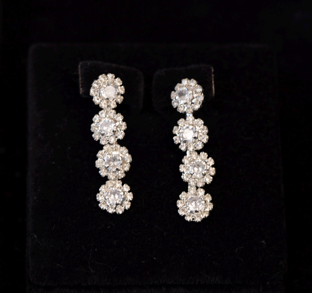 Pair of silver-tone bridal drop earrings, each featuring four small zircon flower clusters, displayed on black velvet.