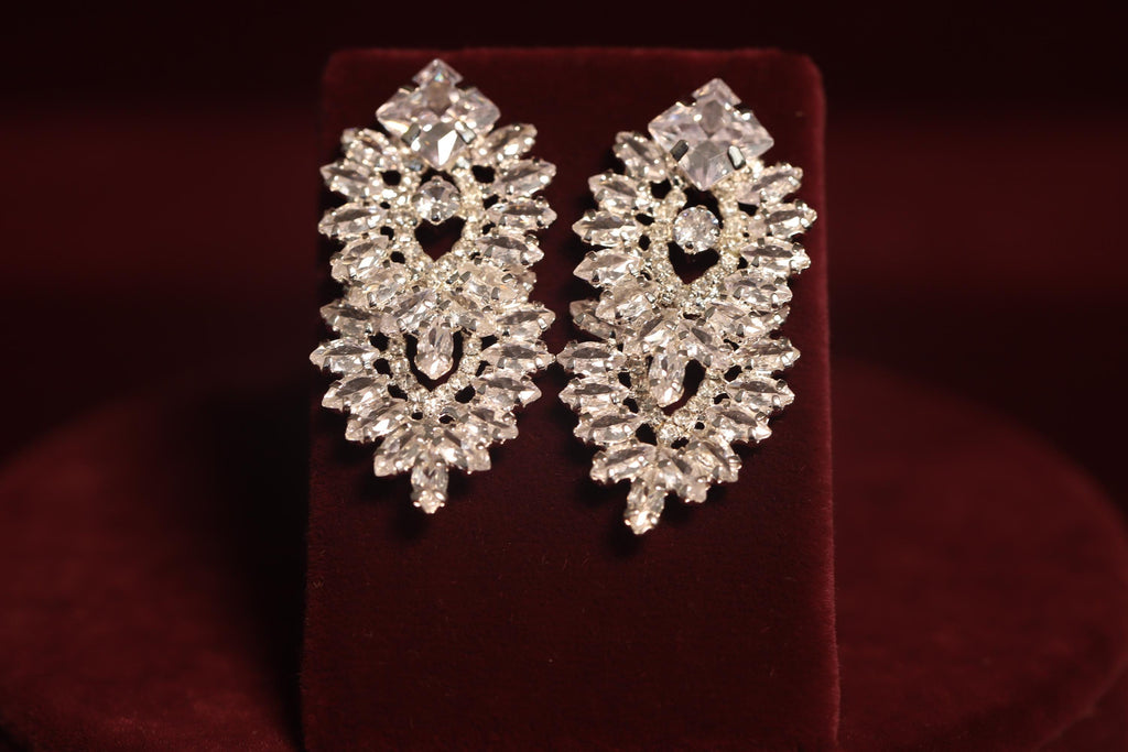 Pair of silver-tone bridal drop earrings with symmetrical marquise-shaped crystal motifs on burgundy velvet
