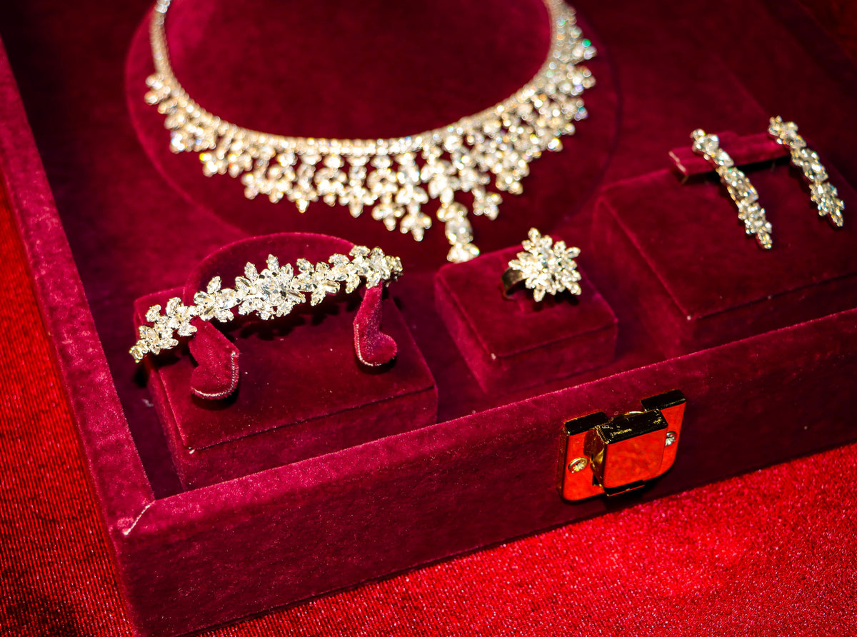 Floral bridal jewelry arranged in a burgundy presentation box, showing the necklace’s leaf motifs and matching accessories.