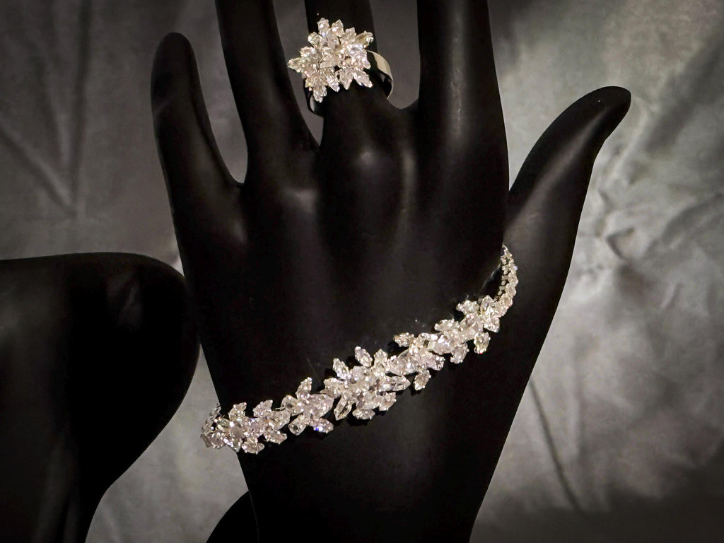 Silver-tone floral bracelet and matching flower ring with clear zircon stones displayed on a black hand stand.