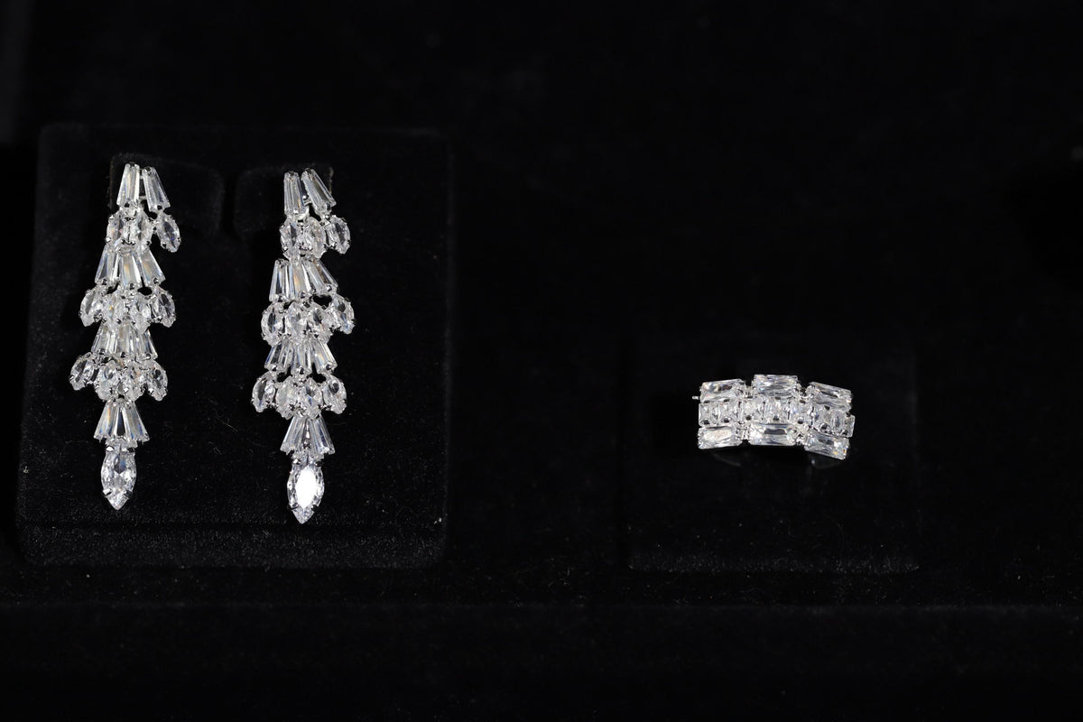 Long baguette zircon bridal earrings with pear-shaped tips and a matching silver-tone ring displayed on black velvet.