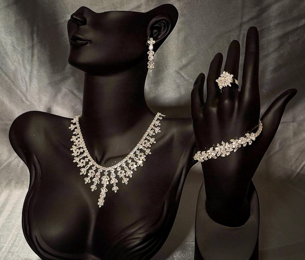 Silver-tone floral bridal jewelry on black display stands, with a teardrop necklace, earrings, bracelet and flower ring.