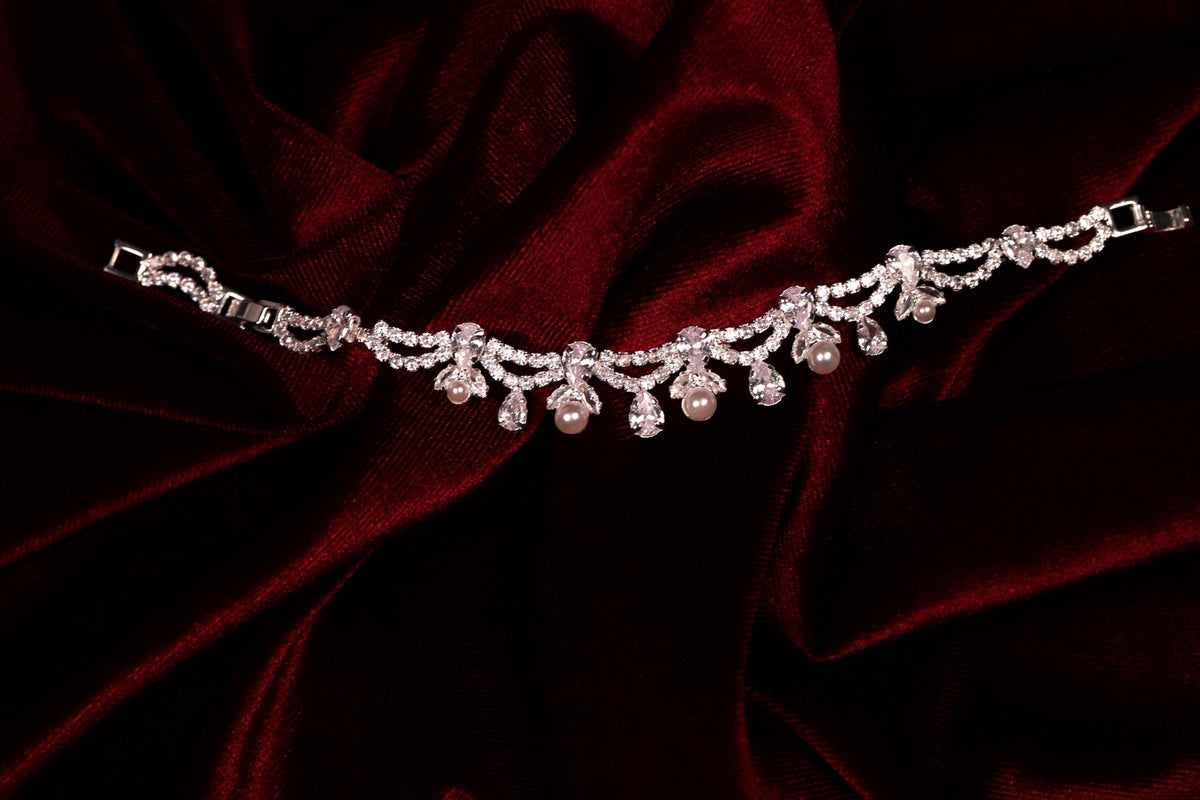 Silver floral crystal bracelet with faux pearl drop details displayed on red satin