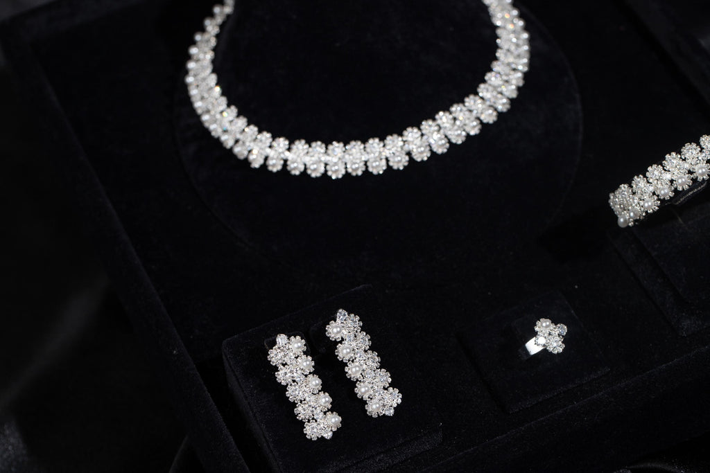 Close-up of a floral faux pearl jewelry set on black velvet, showing the necklace, earrings, ring and part of the bracelet.