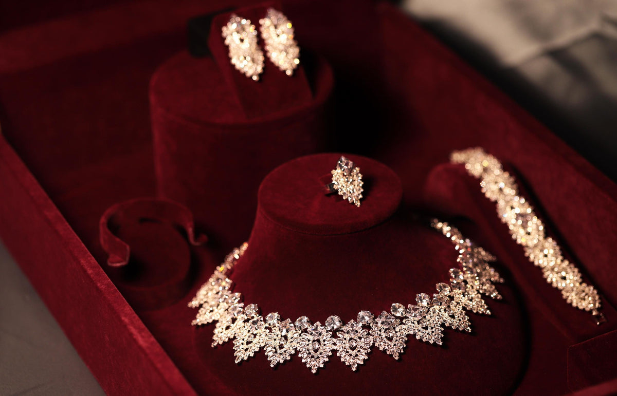 Ornate silver-tone bridal necklace, earrings, bracelet and ring displayed at an angle on burgundy velvet
