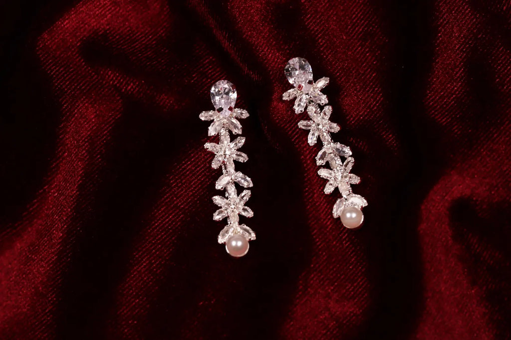 Matching silver cubic zirconia drop earrings with faux pearl accents on red satin