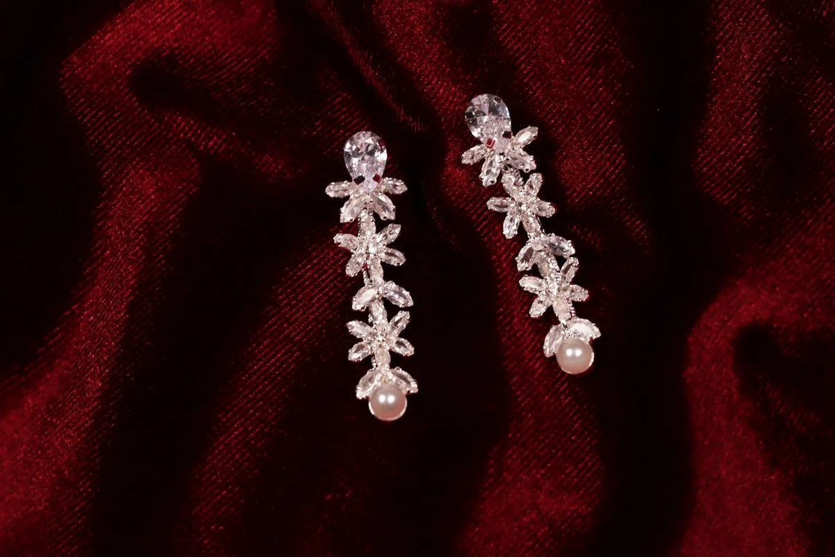 Matching silver cubic zirconia drop earrings with faux pearl accents on red satin