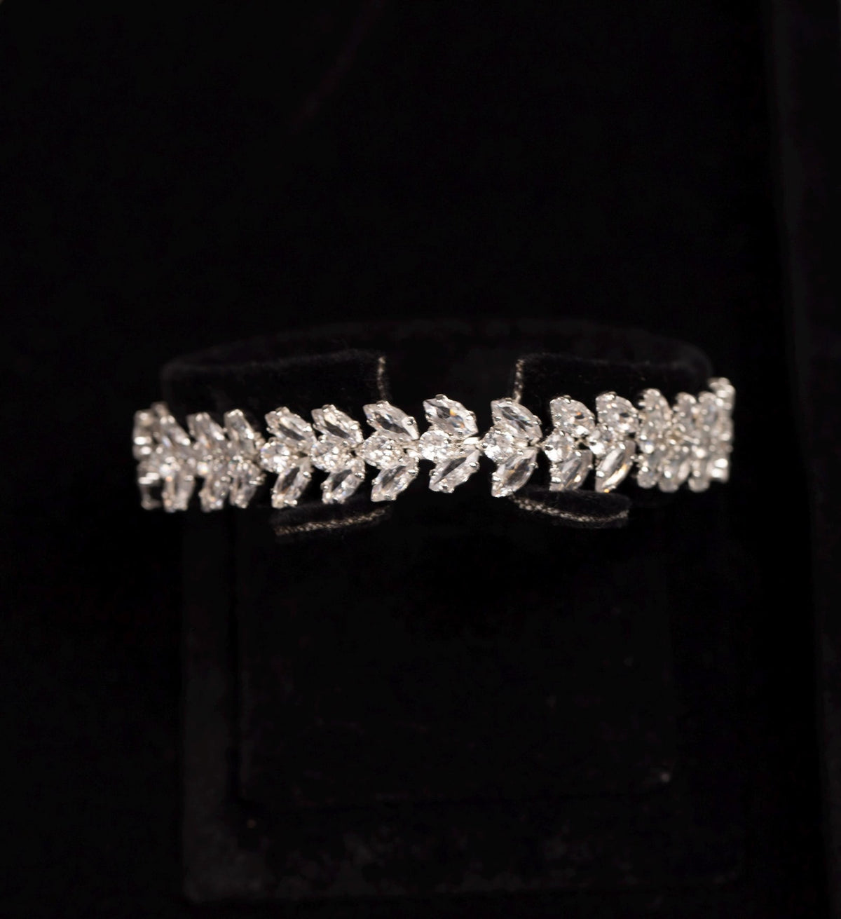 Close-up of a silver-tone zircon bracelet featuring a continuous pattern of paired leaf motifs.