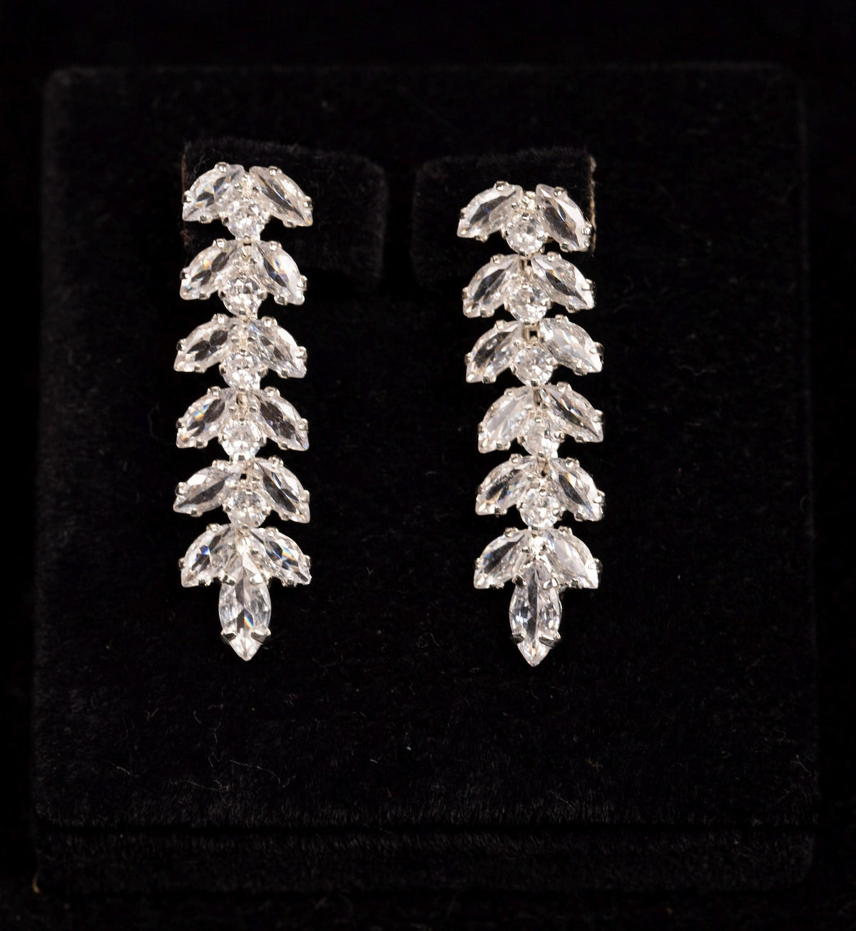 Pair of silver-tone zircon drop earrings with cascading leaf motifs and pointed tips displayed on black velvet.