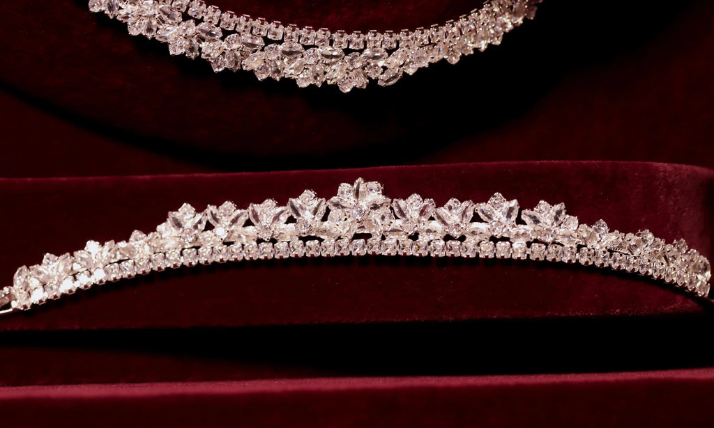 Close-up of a silver-tone zircon bracelet with raised floral motifs and a sparkling stone border on burgundy velvet.