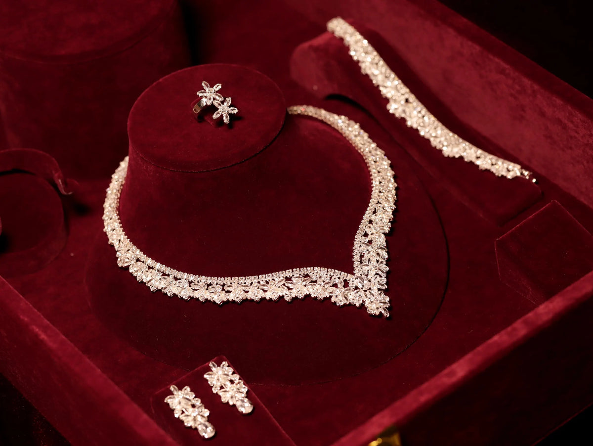 Angled view of a floral V-shaped necklace, matching bracelet, earrings and ring arranged in a burgundy velvet presentation box.