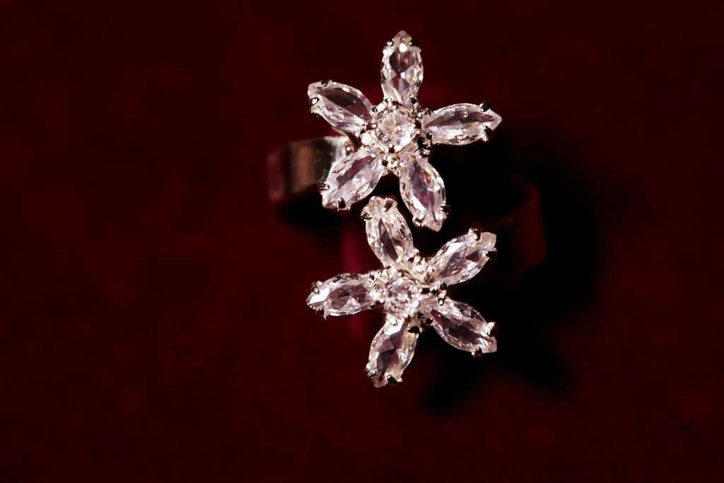 Close-up of a silver-tone ring featuring two zircon flower clusters with pointed petals on a burgundy background.