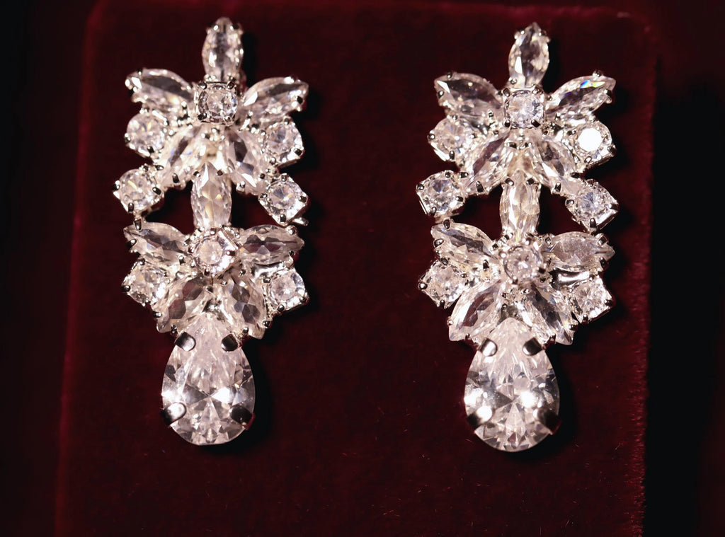 Pair of floral zircon drop earrings with openwork details and pear-shaped dangling stones on burgundy velvet.