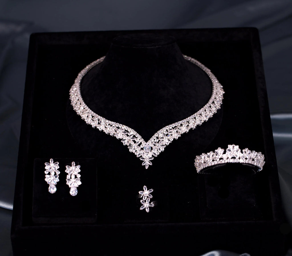 Front view of a floral V-shaped zircon necklace, teardrop earrings, bracelet and flower ring in a black velvet box.